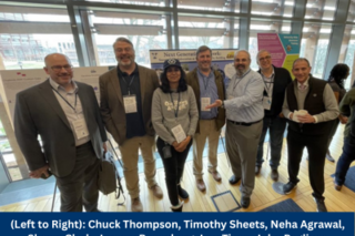 A group of 7 NGN team members stand in front of the NGN team's poster