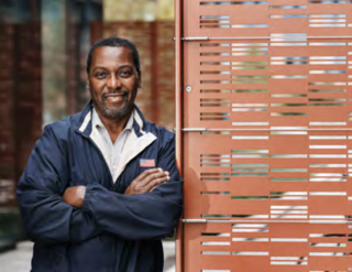 David Highsmith leaning against a wall with his arms crossed, smiling