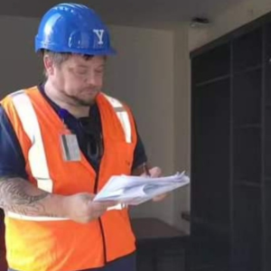 Bob in a hard hat and orange vest surveying a building